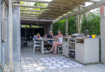 Zwei Personen sitzen an einem Outdoor-Tisch unter einer Pergola im Lodge 2 und 3, 7Huizen aan Zee, Niederlande.