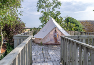 En person træder ud af et telt på en træplatform ved Lodge 2 og 3 på 7Huizen aan Zee i Holland.