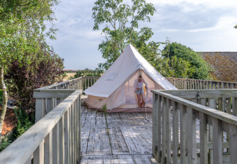 En person træder ud af et telt på en træplatform ved Lodge 2 og 3 på 7Huizen aan Zee i Holland.