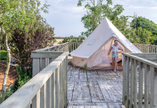 Ein Kind verlässt ein Zelt auf einer Holzterrasse, umgeben von Bäumen, bei Lodge 2 und 3, 7Huizen aan Zee, Niederlande.
