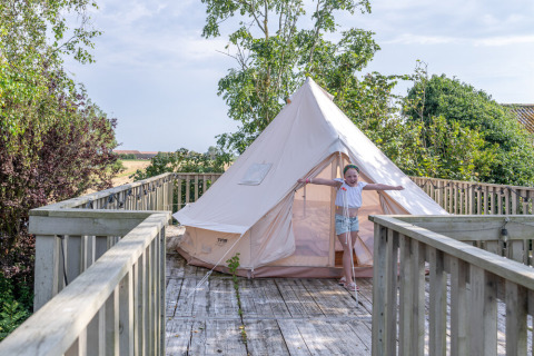 Kind steht vor einem weißen Zelt auf einer Holzterrasse in Lodge 2 und 3, 7Huizen aan Zee, Niederlande.