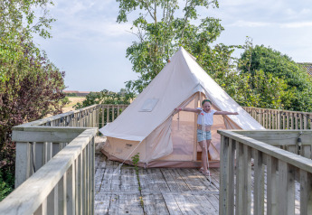 Bambino davanti a una tenda bianca su una terrazza di legno a Lodge 2 e 3, 7Huizen aan Zee, Paesi Bassi.