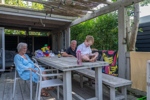 Familie entspannt auf Terrasse von Lodge 2 und 3, 7Huizen aan Zee in den Niederlanden im Sommer.