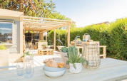 Terrazza soleggiata con tavolo in legno, piante e lanterna presso Lodge 1 e 4 di 7Huizen aan Zee, Paesi Bassi.