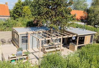 Außenansicht von Lodge 1 und 4 bei 7Huizen aan Zee in den Niederlanden, mit Terrasse und viel Grün.