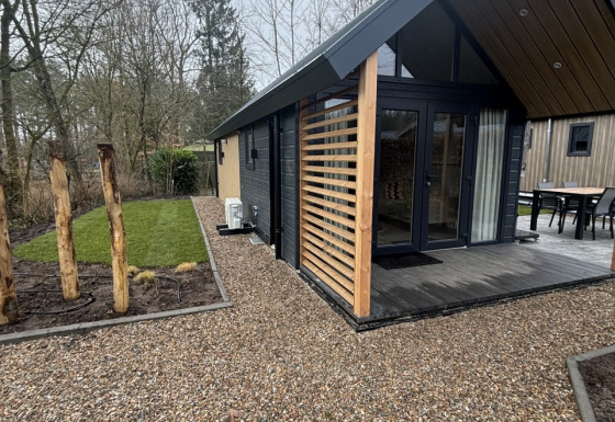 Moderne tiny house ved Veluwepark de Bosgraaf i Holland, med grussti og grønne omgivelser.