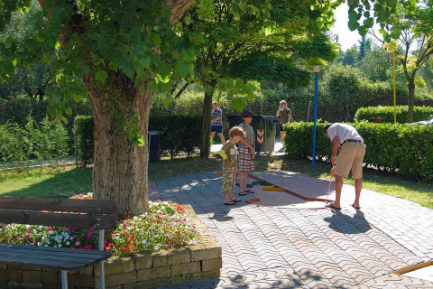 Familia jugando al mini golf bajo un árbol en el Camping Cisano/San Vito en Veneto, Italia.