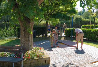 Famiglia che gioca a minigolf sotto un albero al Camping Cisano/San Vito, parco vacanze in Veneto, Italia.