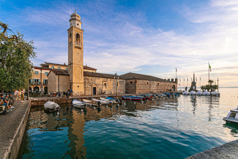 Waterfront in Cisano di Bardolino, Veneto, Italy, showing boats, bell tower, historic buildings, and serene lake.