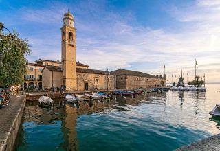 Havneområde i Cisano di Bardolino, Veneto, Italien, med både, klokketårn, historiske bygninger og roligt vand.