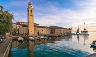 Waterfront in Cisano di Bardolino, Veneto, Italy, showing boats, bell tower, historic buildings, and serene lake.