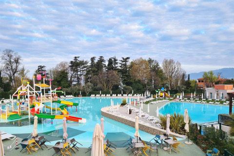 Stor swimmingpool med farverige rutsjebaner og liggestole på Camping Cisano/San Vito i Veneto, Italien.