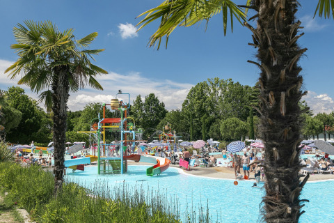 Piscina del campeggio con scivoli d’acqua, palme e famiglie a Camping Cisano/San Vito in Veneto, Italia.
