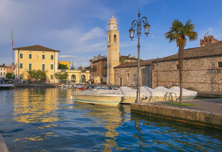 Både og historiske bygninger ved havnen i Camping Cisano/San Vito, Veneto, Italien på en solrig dag.