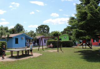 Bambini e famiglie giocano tra bungalow colorati e area giochi al Camping Cisano/San Vito, Veneto, Italia.