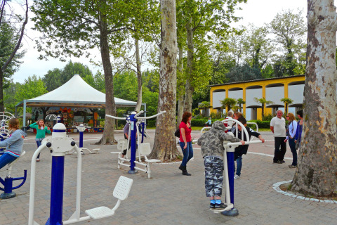 Zona de ejercicio al aire libre en un parque vacacional con personas usando equipos de gimnasia entre árboles.