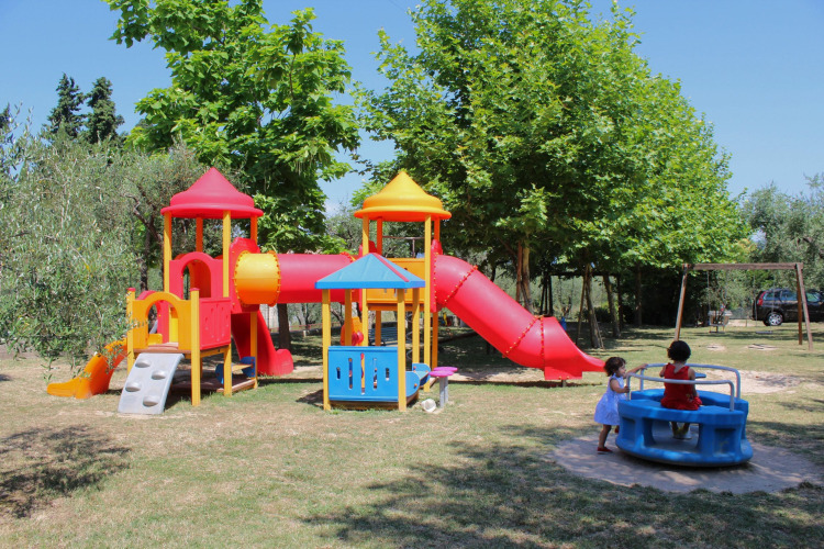Children playing on colorful playground equipment at Camping Cisano/San Vito holiday park in Veneto, Italy.