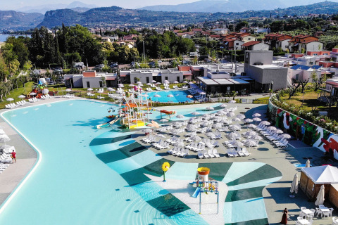 Vista aérea de Camping Cisano/San Vito en Véneto, Italia, mostrando piscinas, tumbonas y sombrillas blancas.