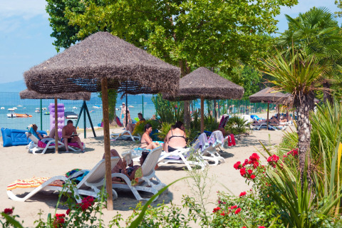 Persone rilassate su lettini sotto ombrelloni di paglia a Camping Cisano/San Vito, Veneto, Italia.