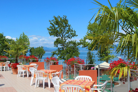 Terrazza esterna al Camping Cisano/San Vito in Veneto, Italia, con vista lago e fiori colorati.