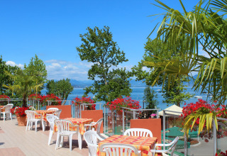 Terrazza esterna al Camping Cisano/San Vito in Veneto, Italia, con vista lago e fiori colorati.