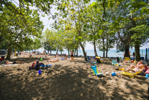 Persone che si rilassano sulla spiaggia ombreggiata dagli alberi a Camping Cisano/San Vito, Veneto, Italia.