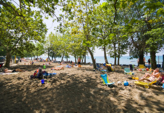 Mensen ontspannen op het met bomen omzoomde strand van Camping Cisano/San Vito in Veneto, Italië.