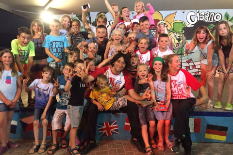 Een grote groep blije kinderen en volwassenen poseert bij Camping Cisano/San Vito, een vakantiepark in Italië.