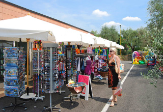 Woman shopping at outdoor market stalls at Camping Cisano/San Vito holiday park in Veneto, Italy.
