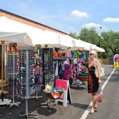 Woman shopping at outdoor market stalls at Camping Cisano/San Vito holiday park in Veneto, Italy.