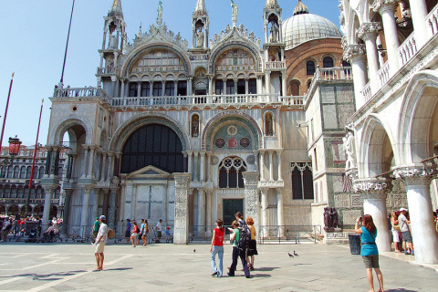Tourists admire an ornate, historic cathedral façade with arches in Veneto, Italy on a sunny day.