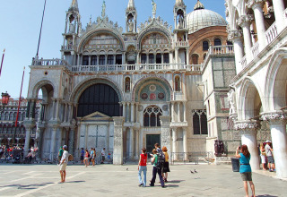 Tourists admire an ornate, historic cathedral façade with arches in Veneto, Italy on a sunny day.