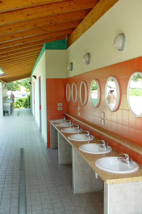 Zona de lavado exterior con espejos redondos y seis lavabos en Camping Cisano/San Vito, Véneto, Italia.