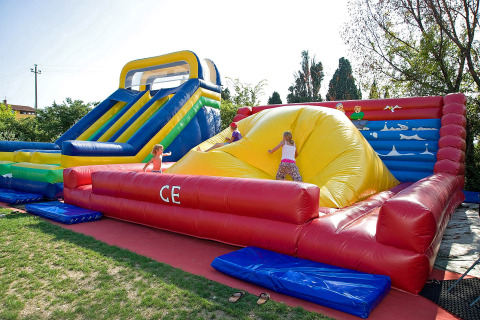 Niños jugando en un gran tobogán hinchable y castillo en Camping Cisano/San Vito, parque vacacional en Véneto, Italia.
