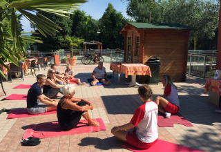 Gruppe udfører udendørs yoga på Camping Cisano/San Vito i Veneto, Italien, under solrige forhold.