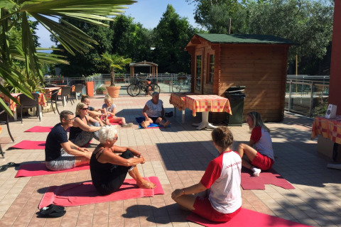 Gruppe udfører udendørs yoga på Camping Cisano/San Vito i Veneto, Italien, under solrige forhold.