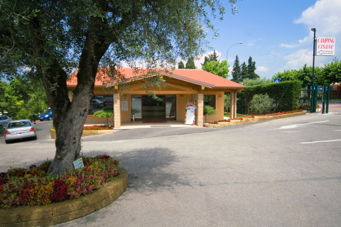 Recepción del Camping Cisano/San Vito en Veneto, Italia, rodeada de jardines, árboles y zona de aparcamiento.