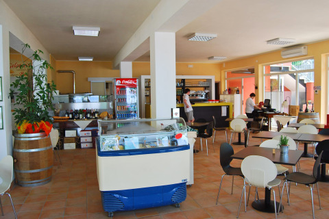 Cafetería luminosa en Camping Cisano/San Vito en Veneto, Italia, con mesas, sillas y mostrador de helados.