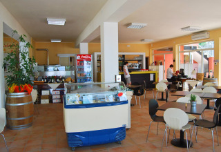 Licht café bij Camping Cisano/San Vito in Veneto, Italië, met tafels, stoelen en een ijsvitrine.