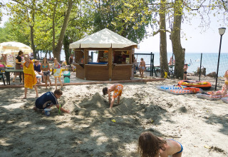 Bambini giocano nella sabbia vicino a un chiosco al Camping Cisano/San Vito in Veneto, Italia.