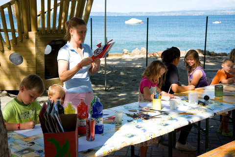 Niños haciendo manualidades en una mesa al aire libre con vista al lago en Camping Cisano/San Vito, Italia.