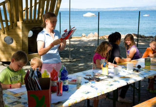 Børn laver kunsthåndværk udenfor ved et bord med udsigt til søen på Camping Cisano/San Vito i Italien.