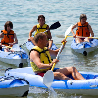 Four people in blue kayaks with life jackets paddling on the water near Cisano di Bardolino, Veneto, Italy.