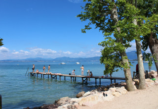 Camping Cisano/San Vito in Veneto, Italia, con pontile, bagnanti e lago soleggiato in una giornata estiva.