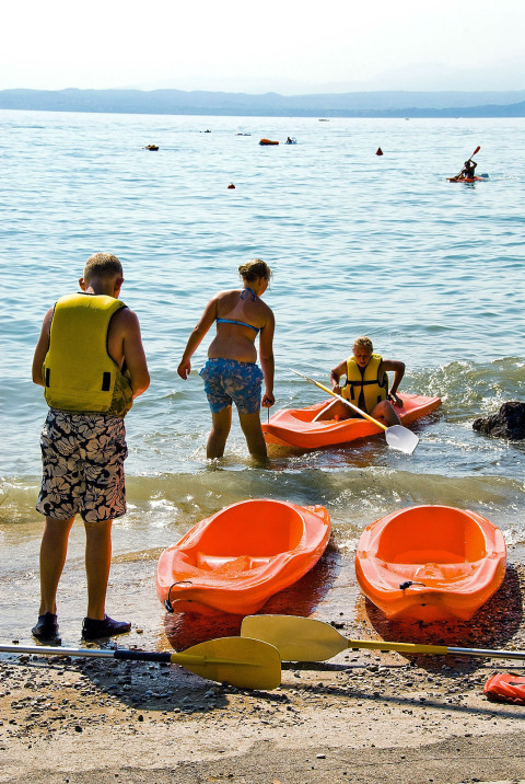 Familia en la orilla del lago en Camping Cisano/San Vito, Véneto, Italia, preparándose para hacer kayak.