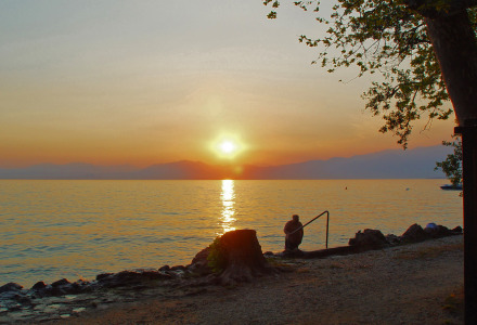 Sunset over Lake Garda near Cisano di Bardolino, Italy, with a person standing at the water’s edge.