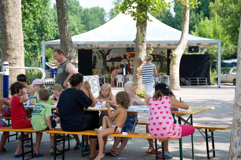 Niños y adultos participan en actividades artísticas en mesas al aire libre en Camping Cisano/San Vito, Veneto.