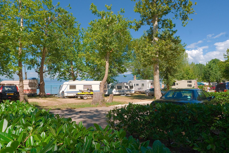 Caravans and cars shaded by leafy trees at Camping Cisano/San Vito holiday park in Veneto, Italy.