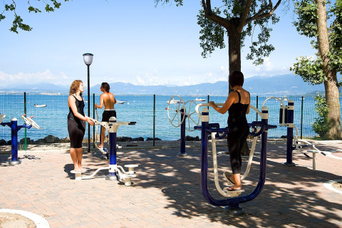 Personas haciendo ejercicio en un gimnasio al aire libre junto al lago en Camping Cisano/San Vito, Veneto, Italia.
