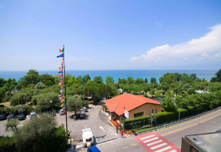 View of Camping Cisano/San Vito holiday park in Veneto, Italy, showing sea, trees, flags, and sunshine.